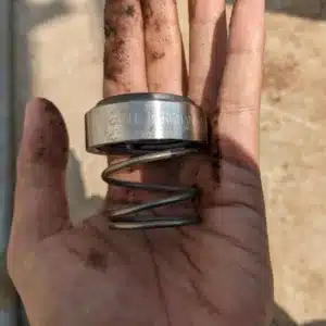 Greasy hand holds metal parts, inspecting for early signs of mechanical seal failure damage